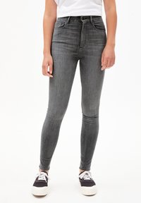 Jeans skinnies grises de cintura alta, con un diseño clásico de cinco bolsillos, cierre de cremallera y un ligero desgaste para mayor textura. Combinados con zapatillas negras.