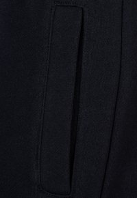 Marineblaue Jogger aus einem weichen, strukturierten Strickstoff. Verfügt über eine Seitentasche mit einem eleganten, minimalen Design. Sichtbare Nähte.