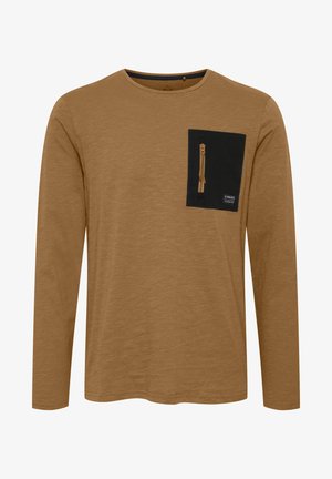 Langermet skjorte i et lysebrunt stoff, med en svart lomme med glidelås og en liten logoetikett nederst på lommen.