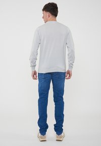 Maglietta a maniche lunghe grigia chiara con colletto tondo, abbinata a jeans in denim blu e calzature di colore chiaro. Design semplice, texture liscia.