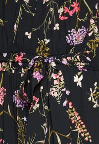 Tissu noir avec un motif floral comportant des fleurs roses, violettes et blanches. Comprend un détail de taille nouée et une texture plissée.