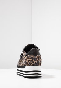 Niski sportowy but z lwim wzorem, czarnym skórzanym obcasem, bocznym zamkiem błyskawicznym i czarno-białą pasekową podeszwą na białej powierzchni.