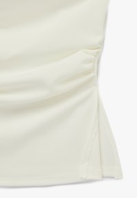 Tela blanca con detalle fruncido y abertura lateral, mostrando textura y costuras en un material ligero y suave.