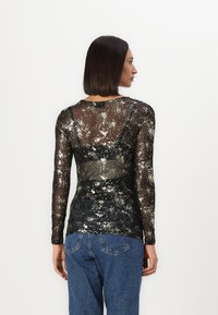 Svart langermet topp med gjennomsiktig stoff som har et gullmetallisk sprutmønster. Slim fit, rund halslinje og gjennomsiktig bakdesign.
