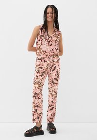 Ärmelloser Overall in Rosa mit einem floralen Muster in Braun- und Schwarztönen. Hergestellt aus leichtem Stoff mit einem elastischen Bund.