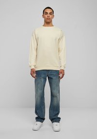 Cream-colored sweatshirt with a wide neckline and dropped shoulders, paired with light blue denim jeans and white sneakers.