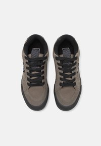 Adidași gri din suede cu tălpi din cauciuc negru, având șireturi negre și un limbaj de material cu etichetă logo. Textură netedă și design casual.