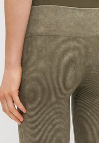 Leggings côtelés vert olive avec une taille haute, une texture douce et des rayures verticales pour une apparence structurée.