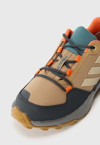 Brun och grå utomhussko med andningsbart mesh-ovandel, orange detaljer, texturerad gummisula och kontrasterande blå krage.
