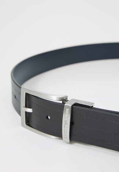 Curea din piele neagră cu o textură netedă, cataramă din metal argintiu și logo-ul mărcii embosat. Are un design clasic cu găuri ajustabile.