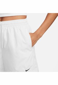 Pantaloni corti bianchi con vita elastica, tasche laterali, tessuto leggero e un piccolo logo nero Nike vicino all'orlo.