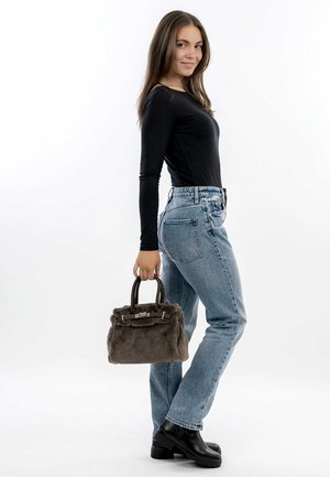 Borsa a tracolla in pelliccia marrone con un design strutturato e doppi manici superiori. Indossata con jeans azzurri a vita alta e stivali neri con tacco spesso.