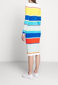Abito midi a maglia con strisce blu, gialle, verdi e rosse, dotato di maniche lunghe e texture a coste, abbinato a sneakers bianche.