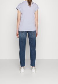 Camiseta de algodón de color lila claro con mangas cortas, combinada con unos vaqueros de denim azul con ajuste recto y diseño de cinco bolsillos. Se llevan zapatillas blancas.