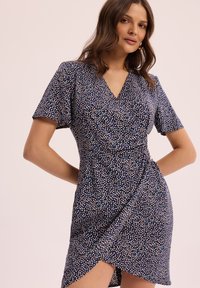 Sukienka kopertowa w granatowym materiale z rozproszonym wzorem kolorowych kropek. Krótkie rękawy i dekolt w serek, z bocznym rozcięciem.