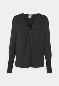 Blusa nera a maniche lunghe con scollatura a V e dettaglio nodo sul davanti. Realizzata in tessuto liscio, con polsini aderenti e una silhouette morbida.