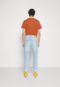Zgorela oranžna majica, svetlo modri široki jeans, rumeni športni čevlji s krožnim vzorcem in tan usnjeni vonj na jeansu.