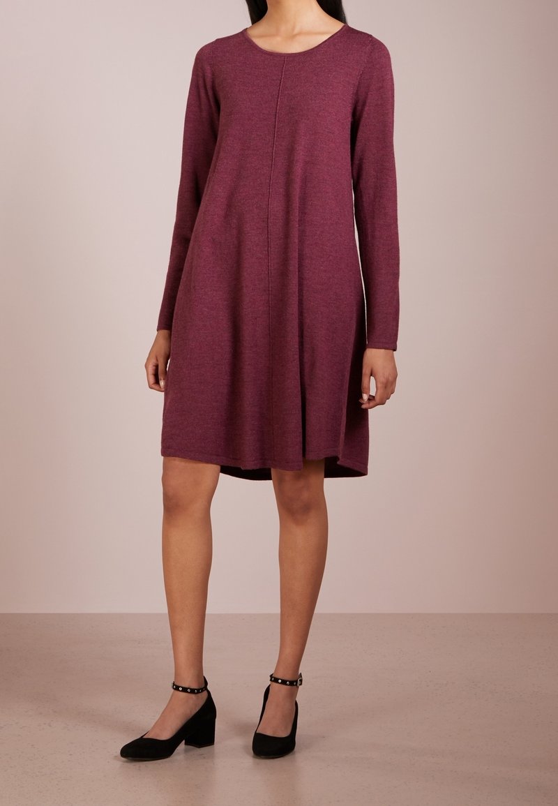 Femme portant une robe bordeaux mi-longue à manches longues avec un col rond et des chaussures noires à talons blocs et brides à la cheville.