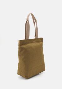 Torba płócienna w oliwkowym kolorze z beżowymi nylonowymi ramiączkami. Posiada kwadratowy kształt i bezszwowy design, idealna do noszenia codziennych niezbędników.