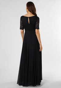 Lang zwart kledingstuk met een kanten lijfje, korte kanten mouwen en een sleutelgatdetail op de rug. De rok valt soepel naar de vloer en heeft een gladde textuur.