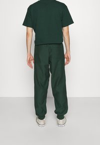 Grön bomull t-shirt och matchande lösa byxor. Byxorna har en bakficka, och båda har en mjuk textur och enkel design.