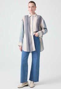 Koszula z paskami w beżowych i niebieskich odcieniach, w połączeniu z niebieskimi spodniami typu wide-leg i jasnym obuwiem. Gładka tekstura i casualowy design.