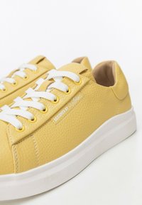 Sneaker in pelle gialla con lacci bianchi, superficie texturizzata e suola bianca. Presenta il marchio "Designed by Witchen" sul lato.