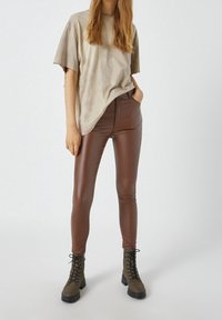 T-shirt oversize marron clair à la texture douce, associée à des leggings marron brillants et ajustés, et des bottines vertes à lacets avec semelles noires.