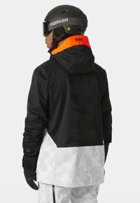 Schwarz-weiße Schneejacke mit orangefarbener Akzentuierung an der Kapuze, mit einem strukturierten Rückenmuster und verstellbaren Bündchen.