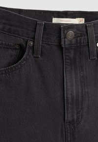 Črne denim hlače s klasičnim krojem, ki imajo pet žepov, kovinsko zaponko in design s cinčanim pasom. Tekstura je gladka z rahlim leskom.