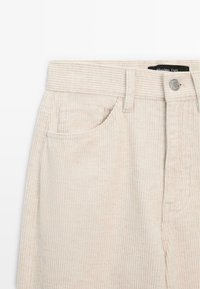 Beige corduroy pants with vertical stripes, featuring a front pocket, metal button closure, and a label at the waistband.