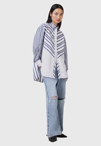 Skjorte med knaplukning lavet af letvægtsbomuld, med blå og hvide diagonale og lodrette striber. Kombinationen med slidte blå jeans og sorte sko.