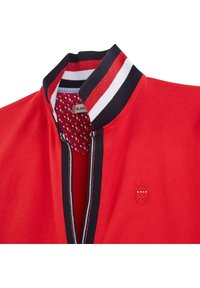 Veste zippée rouge avec un col côtelé aux rayures bleu marine, blanc et rouge, et une doublure intérieure texturée à motif. Détail du logo brodé.
