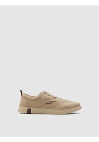 Zapato beige con cordones hecho de material sintético suave. Presenta un cuello acolchado, un sutil logo y un acento oscuro contrastante en el talón.