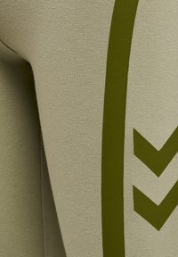 Olijfgroene sportleggings van rekbaar materiaal, met een groot, gedurfd pijlontwerp in een donkerdere tint aan de zijkant.
