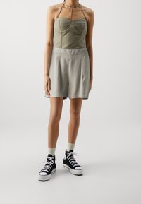 Olivengrøn bustier-top med strukturerede syninger, parret med lysegrå plisserede shorts. Båret med sorte høje sneakers og lyse sokker.