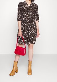 Svart klänning med djurmönster, 3/4 ärmar; matchad med en röd handväska och beige klackstövlar, slät textur genomgående.