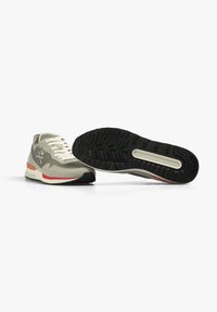 Beige Sneaker mit strukturiertem Obermaterial, hellgrauen Überzügen, schwarzer Sohle und einem orangefarbenen Akzent an der Ferse. Verfügt über Schnürsenkel und ein Logodetail.