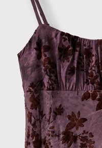 Gros plan d'une robe violette à fines bretelles avec un motif floral en velours floqué foncé sur un tissu texturé.