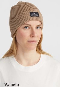Brown ribbed beanie with a black O'Neill logo patch; worn snugly, highlighting textured knit fabric, suitable for cold weather.