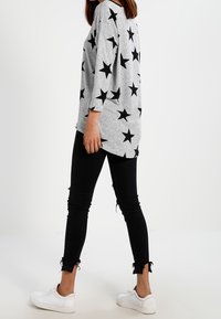 Chemise grise à manches longues avec un motif d'étoiles noires, associée à un jean skinny noir avec des bords effilochés et des baskets blanches.