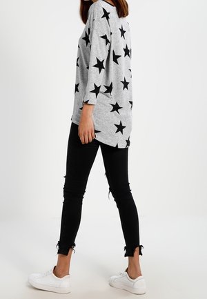 Chemise grise à manches longues avec un motif d'étoiles noires, associée à un jean skinny noir avec des bords effilochés et des baskets blanches.