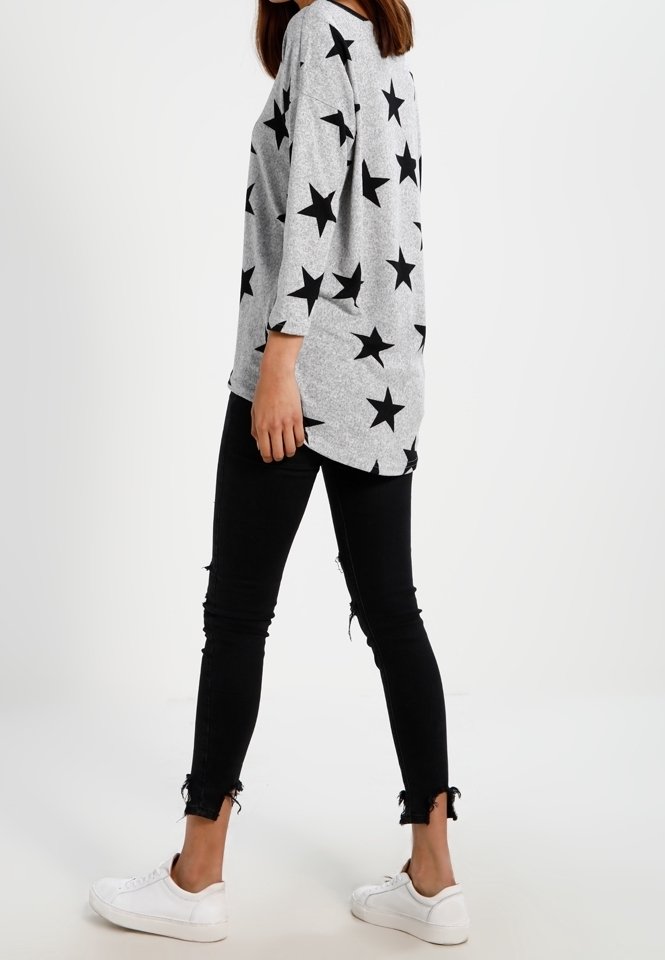 Chemise grise à manches longues avec un motif d'étoiles noires, associée à un jean skinny noir avec des bords effilochés et des baskets blanches.