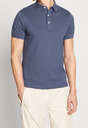 Granatowa koszulka polo z bawełny, z klasycznym kołnierzykiem, rozcięciem na trzy guziki i małym logo na klatce piersiowej. Teksturowane wykończenie tkaniny.