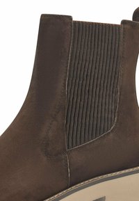 Brown suede ankle boot featuring a ribbed elastic panel, a rounded toe, and a contrasting light-colored sole with stitching details.