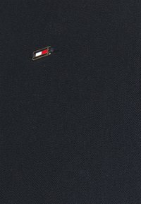 Marinblått tyg med en strukturerad yta har en liten guldfärgad pin som visar en röd, vit och blå logotyp i ett rektangulärt mönster.