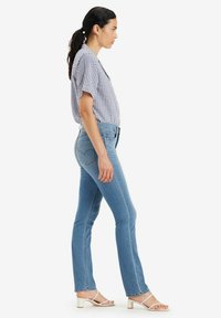 Jeans in denim blu con vestibilità slim, lavaggio chiaro e cuciture a forma di cuore sulle tasche posteriori, abbinati a una camicia a maniche corte con motivo a quadretti.