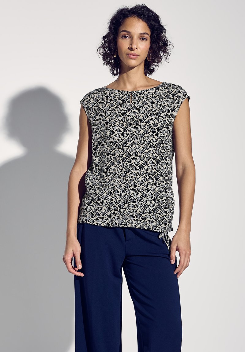 Top a maniche corte in blu navy e crema con un motivo floreale e un dettaglio di nodo laterale, abbinato a pantaloni blu navy a vestibilità ampia.