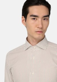 Camisa de botones a rayas con finas rayas marrones sobre un fondo crema, con un cuello clásico y una tela texturizada.
