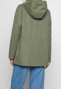 Olivově zelená nepromokavá bunda s kapucí, nastavitelným pasem a dlouhými rukávy. Hladký povrch, dokončeno viditelnými švy.
